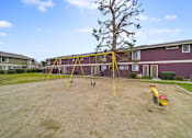 Thumbnail 10 of 18 - A playground with a yellow swing set and a red slide in front of a red building.