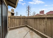 Thumbnail 15 of 18 - A concrete patio with a wooden fence and a tree in the background.