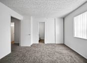 Thumbnail 9 of 21 - A room with white walls and a carpeted floor with a window on the right side.