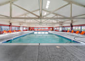 Thumbnail 1 of 21 - A large indoor swimming pool with a blue water surface and orange chairs around the pool.
