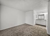 Thumbnail 3 of 21 - A room with a carpeted floor and a small kitchenette in the corner.