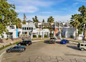 Thumbnail 3 of 18 - A parking lot with cars and a building in the background.