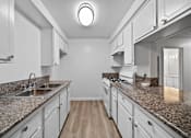 Thumbnail 6 of 10 - A kitchen with granite countertops and white cabinets.