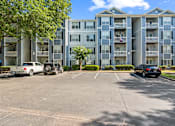 Thumbnail 22 of 22 - A black car is parked in a parking lot in front of a large apartment building.