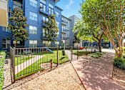 Thumbnail 9 of 19 - A tree-lined walkway leads to a gated courtyard with a playground at The Atlantic Highland Park, TX