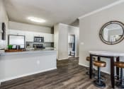 Thumbnail 8 of 25 - a living room with a kitchen and a bar with stools at Village of Hawks Creek Apartments, Westworth Village, TX