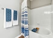 Thumbnail 10 of 24 - A white bathtub with a blue and white shower curtain.