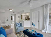 Thumbnail 20 of 23 - A living room with a grey couch, a blue ottoman, and a white ceiling fan at Boca Colony Apartments, Boca Raton, FL