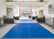 Thumbnail 14 of 34 - A blue ping pong table is in the middle of a room with a white wall and a painting hanging on i  at The Atlantic Memorial, Houston.