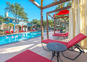 Thumbnail 13 of 34 - A pool area with red lounge chairs and a table at Reserve at Canyon Creek,Texas