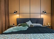 Thumbnail 2 of 17 - A bed with a floral comforter and a green pillow is in the foreground of a room with two wall lamps.