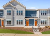 Thumbnail 1 of 30 - a row of houses with orange doors and blue siding at Tivoli Green Apartments & Townhomes, Mount Pleasant, WI