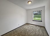 Thumbnail 7 of 28 - A room with a carpeted floor and a window showing a view of a building and trees.