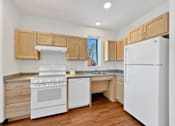 Thumbnail 4 of 46 - An L shaped kitchen at Stryker Senior Apartments in West St. Paul with white appliances and wooden cabinets.