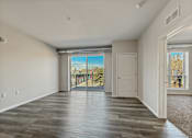 Thumbnail 4 of 31 - A spacious room with wooden flooring and a view of a fenced area outside through a sliding glass door.