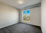 Thumbnail 5 of 31 - A room with a grey carpet and a window showing a view of a tree and a building.
