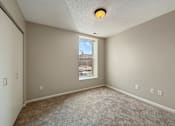 Thumbnail 6 of 15 - A room with a carpeted floor and a window showing a cityscape outside.
