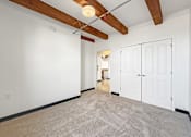 Thumbnail 32 of 34 - A room with white walls and a carpeted floor with a wooden beam ceiling.