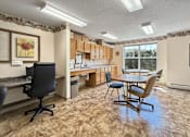 Thumbnail 13 of 16 - A room with a desk, chairs, and a kitchen area.