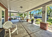 Thumbnail 2 of 16 - A white chair is on a porch with a clock on a post.