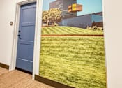 Thumbnail 9 of 37 - A wall mural depicting a building and a field with a blue door in the foreground.