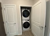 Thumbnail 27 of 31 - A white washing machine is in a small alcove between two doors.