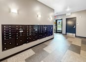 Thumbnail 21 of 22 - A hallway with a wall of mailboxes and a door at the end.