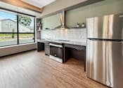 Thumbnail 17 of 22 - A modern kitchen with a stainless steel refrigerator and wooden flooring.