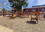 Thumbnail 2 of 29 - A playground with a yellow slide and a red and yellow play structure in front of a Liberty Plaza Townhome building.