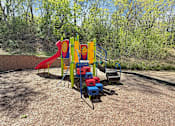 Thumbnail 20 of 20 - A playground with a red slide, a blue and yellow climbing frame, and a red and blue climbing wall.