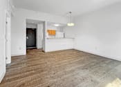 Thumbnail 13 of 27 - A room with wooden flooring and a kitchenette in the background.