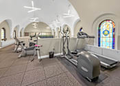 Thumbnail 10 of 27 - A gym with exercise equipment and stained glass windows.