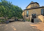 Thumbnail 1 of 27 - A brick building with a black door and windows is surrounded by trees and benches.