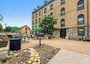 Thumbnail 24 of 27 - A courtyard with a bench, a table, and a trash can.