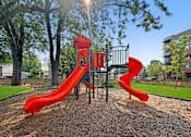 Thumbnail 23 of 27 - A playground with a red slide and a black metal structure.