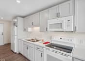 Thumbnail 26 of 58 - A white kitchen with a refrigerator, microwave, oven, and sink.