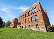 Thumbnail 20 of 20 - A red brick building with a stone foundation and a green lawn in front.