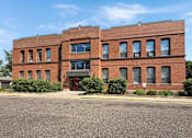 Thumbnail 3 of 20 - A red brick building with a black awning and a parking lot in front.