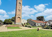 Thumbnail 25 of 28 - A tall tower with a clock on it stands in a grassy area.