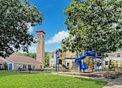 Thumbnail 2 of 28 - A playground with a blue slide and a clock tower in the background.
