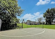 Thumbnail 14 of 28 - A basketball court surrounded by trees and a building in the background.