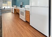 Thumbnail 29 of 35 - A white refrigerator stands in a kitchen with wooden floors and white walls.