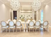 Thumbnail 6 of 21 - A large dining table with white chairs and a chandelier hangs in a spacious room.
