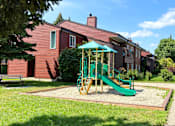 Thumbnail 10 of 12 - A playground with a green slide and a red building in the background.