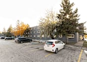 Thumbnail 10 of 12 - A parking lot with a white car parked in front of a grey building.
