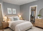 Thumbnail 6 of 27 - A bedroom with a large bed, a nightstand with lamps, a wardrobe, and a small table with a plant on it.