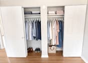 Thumbnail 9 of 10 - A white closet with clothes hanging inside.