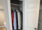 Thumbnail 5 of 10 - A white door is open to a closet with clothes hanging on it.