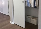 Thumbnail 12 of 27 - A white closet with clothes hanging and baskets on the shelf.