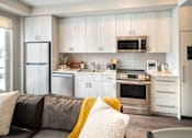 Thumbnail 11 of 30 - A modern kitchen with a grey couch and a yellow throw pillow.
